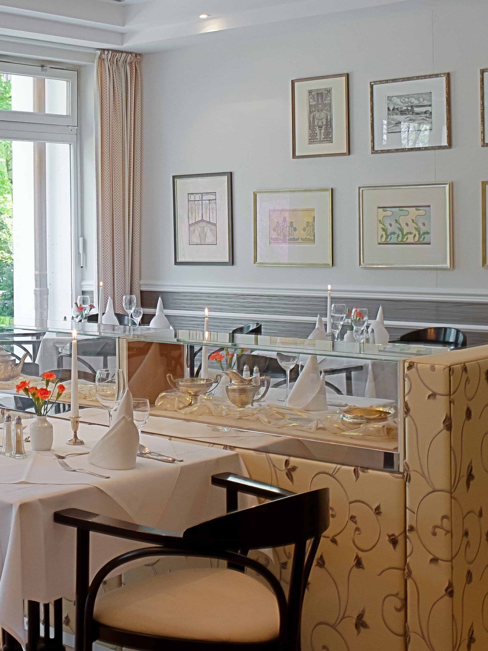 Gedeckter Tisch vor einer Buffet-Vitrine und Wandbildern im Speiseraum